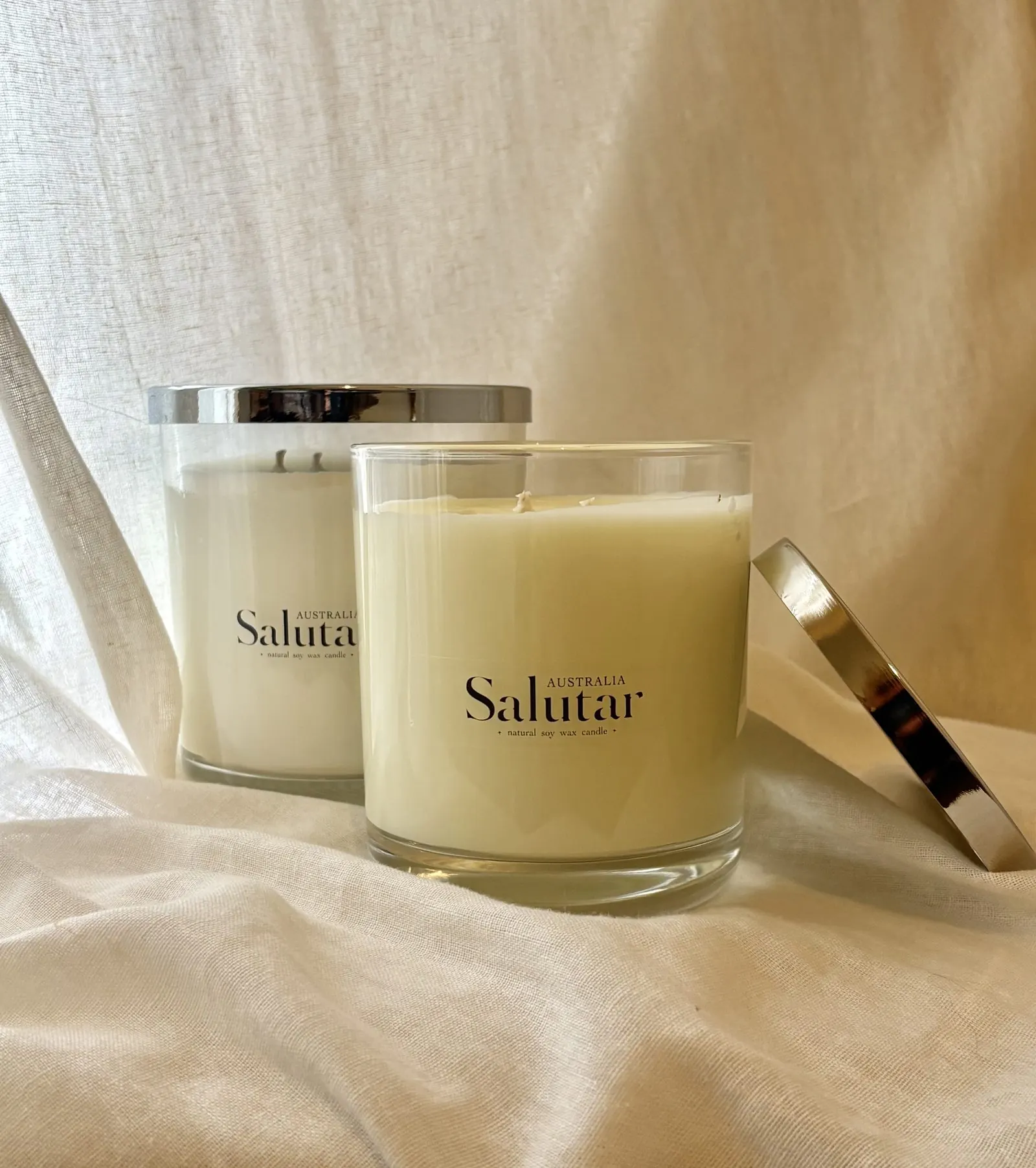 Two Salutar Australia candles, one lit, standing together on natural linen.